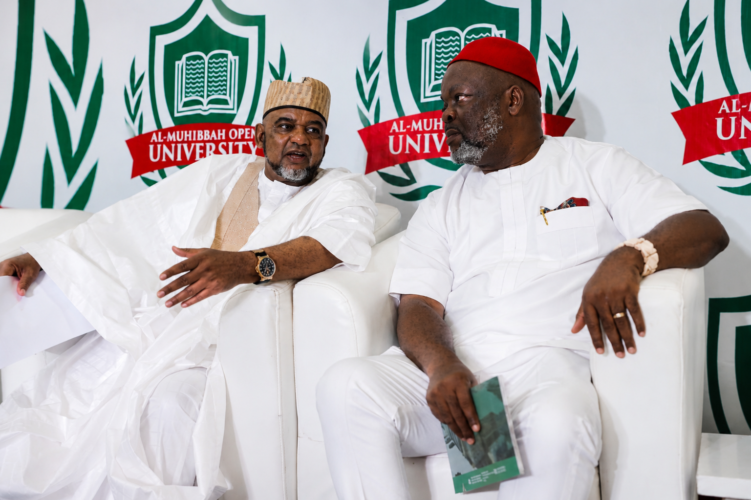 Two men in traditional attire seated at Al-Muhibbah Open University event.